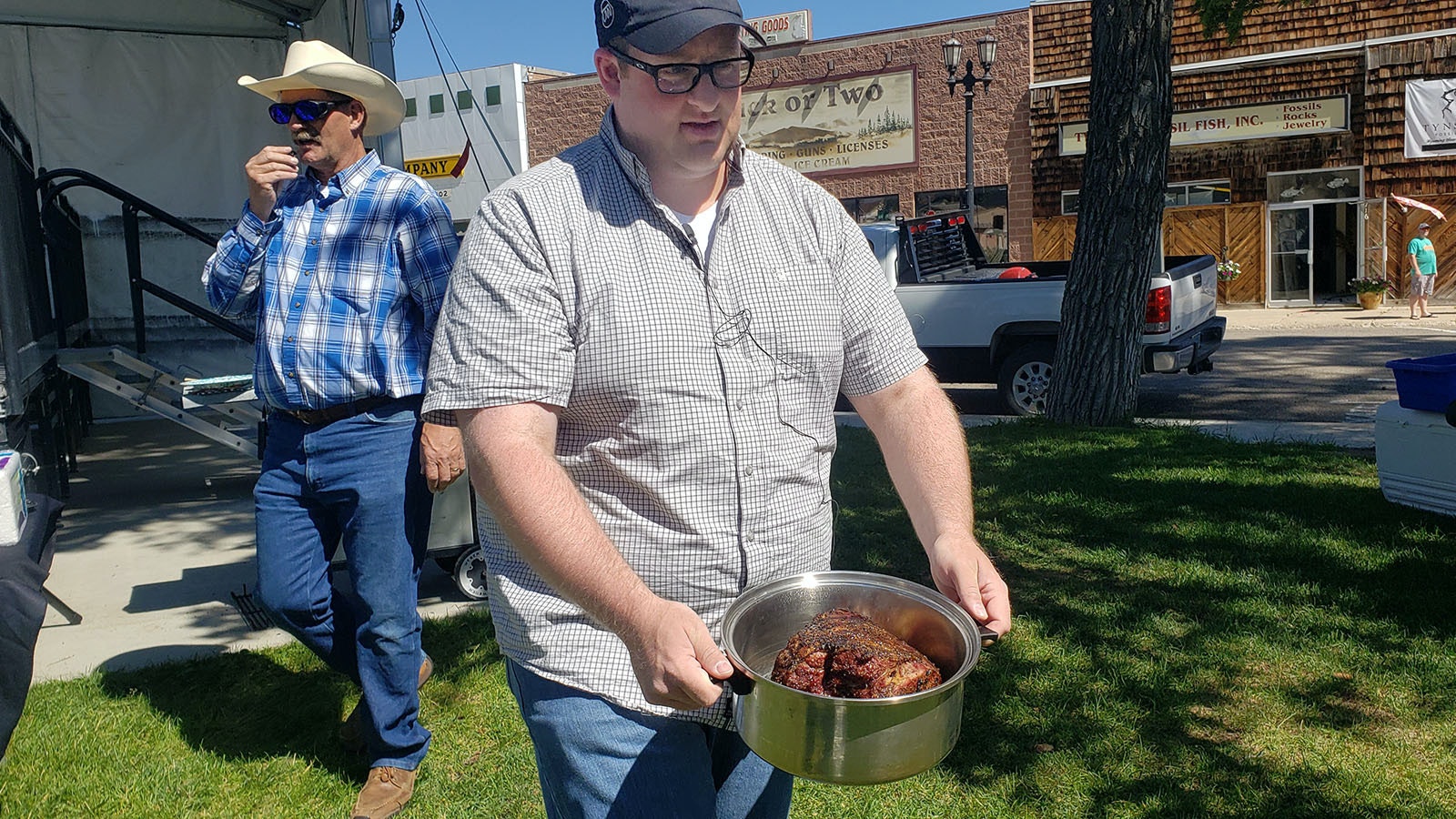 Meat scientist and flavor expert Dr. Cody Gifford front holds a pot of roasted lamb out during a lamb cooking demonstration in Kemmerer recently while meat scientist Dr. Warrie Means, back left, talks about the preparation method.
