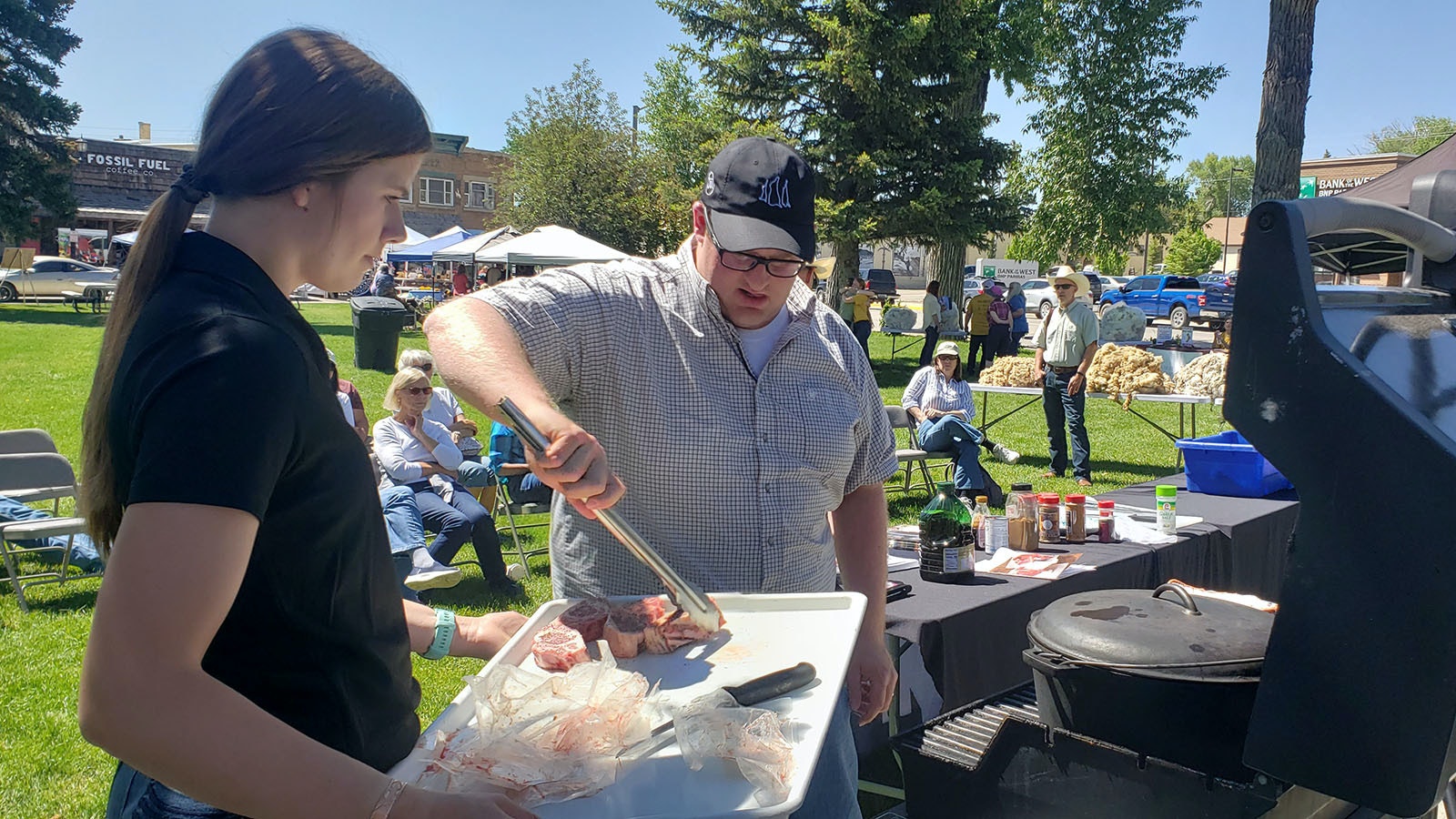Meat scientist and flavor expert Dr. Cody Gifford right places lamb steaks on the grill while a volunteer holds the tray of meat for him.